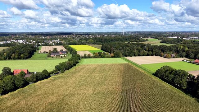 Aerial rising wide shot of american countryside with farmland and cultivated fields in autumn. Dense white clouds at blue sky. Colored trees in fall season. Farmstead in small village of United States