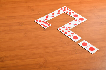 Domino pieces forming a question mark on a wooden table.