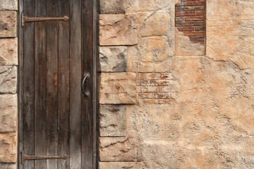 Arabian style house building with closed wooden door and sandstone wall. Building and object photo, close-up.