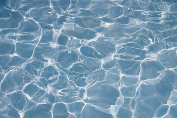 Blue water surface with bright sun light reflections, water in swimming pool background
