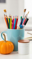 Obraz premium Colorful stationery in a blue cup next to a small pumpkin and a jar on a creative workspace