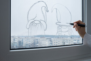 Sustainable responsible holiday decor. Female hand painting gnomes painted on window glass indoor at home. Christmas winter decoration. White pattern. Snow art tracery on season. Diy. Hygge home