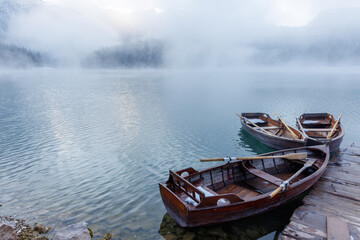 Wooden boats by the pier on a lake at sunset with mist rising over the water