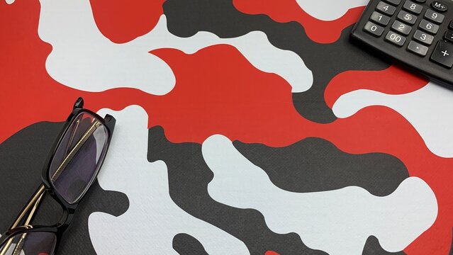 Glasses and calculator on bold red, black, and white pattern suggest focus and financial planning
