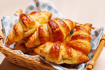 Freshly baked croissants in wicker basket on light background