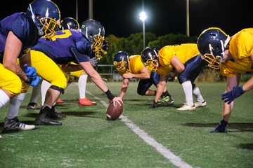 Two American football teams facing off at the line of scrimmage, ready for action under stadium lights