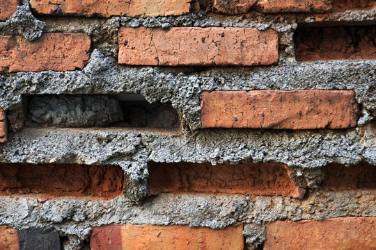 A close-up of an old, weathered brick wall with missing bricks and rough, crumbling mortar, showcasing a rustic and aged texture.