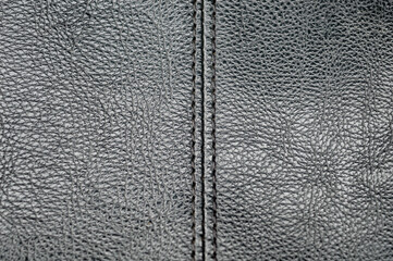 close-up macro of dark gray, black textured leather with a vertical stitched seam. Represents upholstery, fashion, abstract material background, and textile manufacturing detail.