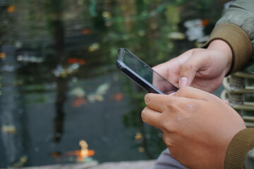 Person Using Smartphone Near Pond With Koi