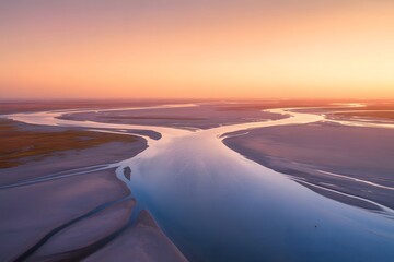Expansive aerial view of a winding river delta at sunset with warm orange and pink sky reflecting on the water and surrounding landscape
