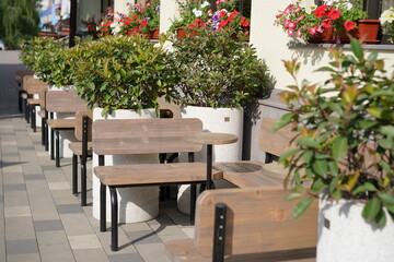 Outdoor seating area with wooden tables and flower pots near a busy street in a sunny afternoon