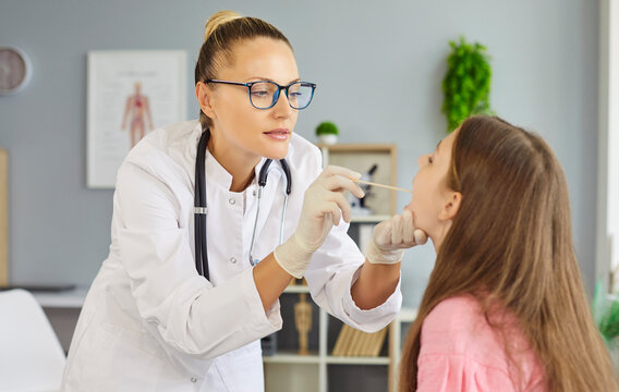 Pediatrician swabs child patient throat for test. The doctor at the clinic conducts an exam, using a sterile swab for diagnosis and screening. Concept: pediatric healthcare and testing.