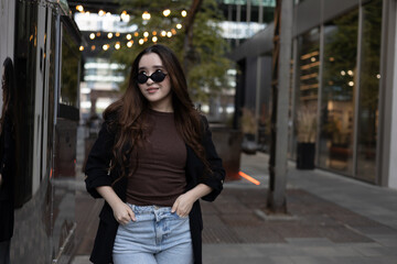 Asian woman in smart-casual blazer and jeans posing by a storefront glass — urban street-style lifestyle portrait