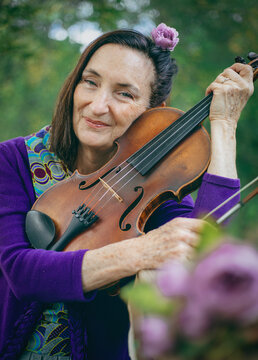 A woman with a flower in her hair holds a violin close to her face