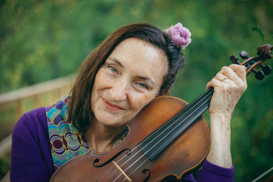 A woman with a flower in her hair holds a violin close to her face