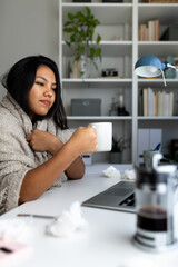 Sick latina woman working from home drinking hot beverage