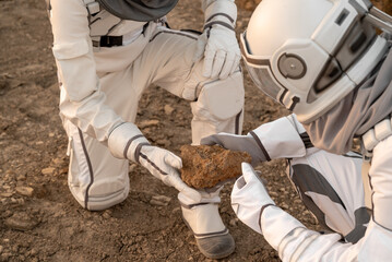 Explorers in astronaut suits holding and observing alien ground samples on the red planet.