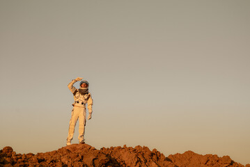 Space mission crew member standing on rocky red planet surface with arm extended in exploration gesture.