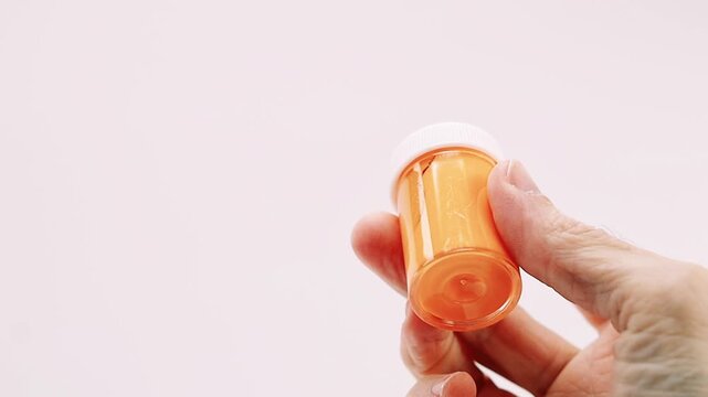 Close-up framing of hand holding and turning an orange acrylic tempera container