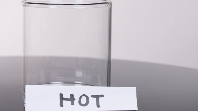 Hand Placing 'HOT' Label Beside Empty Glass Beaker