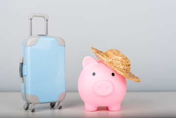 Piggy bank with a straw hat and a suitcase on a minimalist background