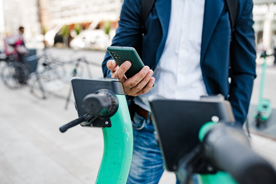 Businessman unlocking electric scooter with smartphone.