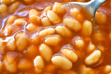 Baked beans in tomato sauce on spoon.
