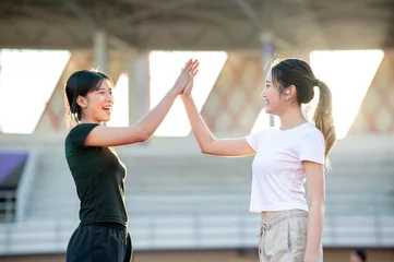 Fotobehang Beren Pretty asian woman in sportswear clapping hands high five with friend while exercising in a stadium.  © bongkarn