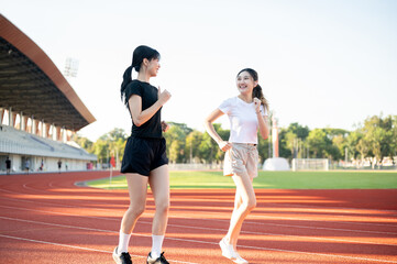 Asian woman and friend talking while running or jogging on racetrack in sports stadium on sunny day.