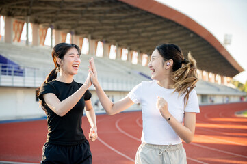 Asian woman clapping hands high five a friend while running jogging on racetrack in sports stadium.