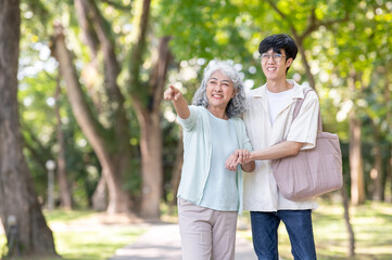 Obraz premium Old woman grandmother pointing and young man grandson supporting as walking together in garden park