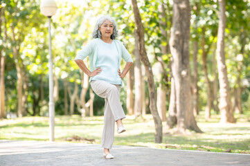 Old age asian woman grandmother put hands on waist raising a leg while walking or exercising in park