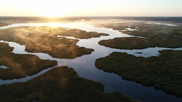 Slow aerial drone shot rising above a misty marsh at tranquil dawn, revealing abstract patterns of water and land scenic, sunrise, drone