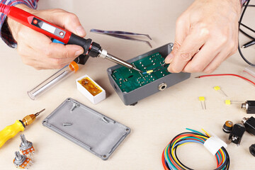Serviceman solder electrical board of device at service workplace.