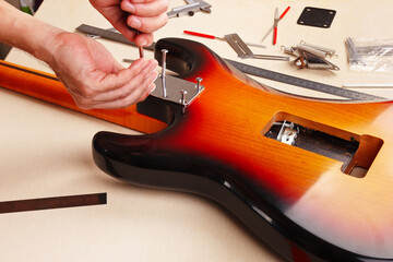 Guitar repairer screws neck on electric guitar.
