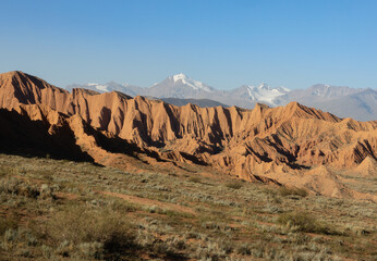 Arid red sandstone landscape and snow-covered mountain peaks in the background of majestic Issyk-Kul region nature in Kyrgyzstan