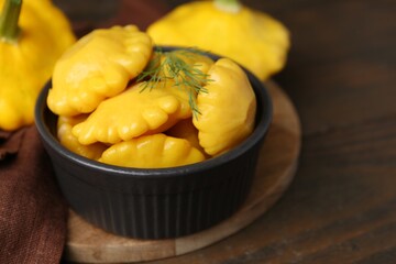 Pickled pattypan squashes in bowl and fresh vegetables on wooden table, closeup. Space for text