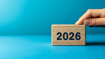 This photo shows hands stacking wooden blocks. The blocks bear the year "2026."