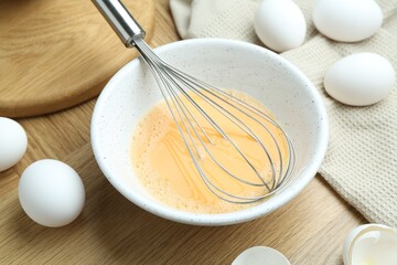 Beaten eggs in bowl and whisk on wooden table, closeup