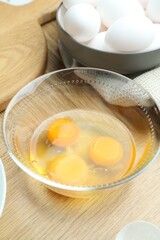 Raw eggs and yolks in glass bowl on wooden table, closeup
