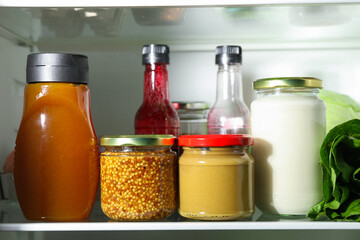 Bottles with different tasty sauces in fridge, closeup