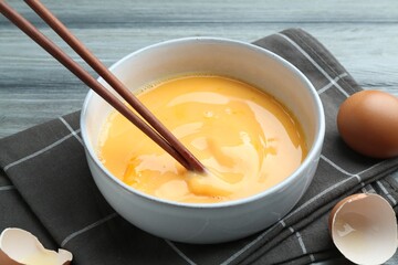 Beaten eggs in bowl and chopsticks on table, closeup