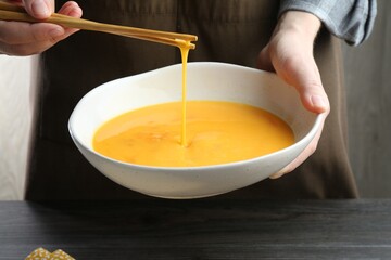 Woman whisking eggs in bowl at dark wooden table, closeup