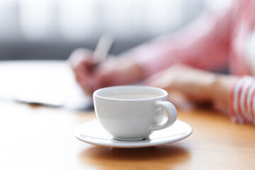 Coffee break. Woman writing at wooden table indoors, focus on cup