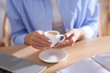 Woman having coffee break at wooden table indoors, closeup