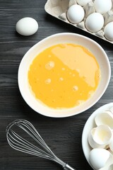 Beaten eggs in bowl and whisk on dark wooden table, flat lay