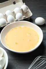Beaten eggs in bowl and whisk on dark wooden table, closeup