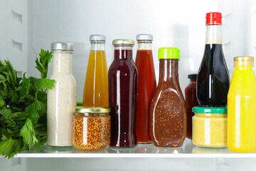 Bottles with different tasty sauces and products in fridge, closeup