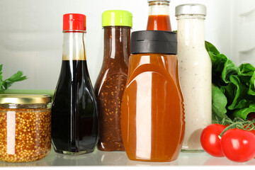 Bottles with different tasty sauces and products in fridge, closeup
