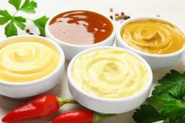 Different tasty sauces in bowls, parsley, peppercorns and chili peppers on white wooden table, closeup